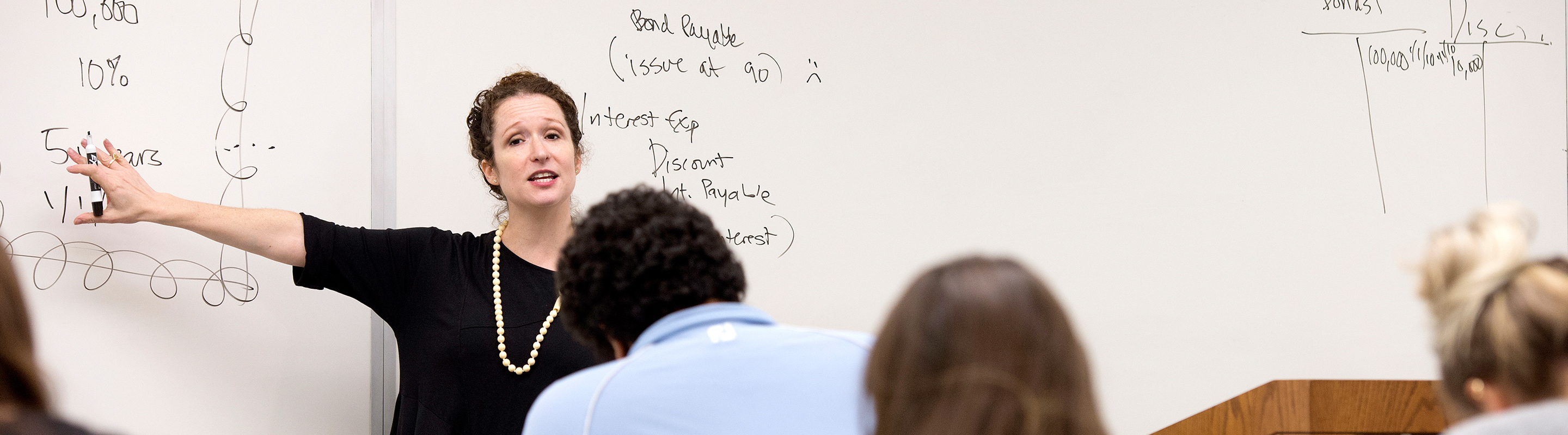 Professor pointing to whiteboard in accounting class